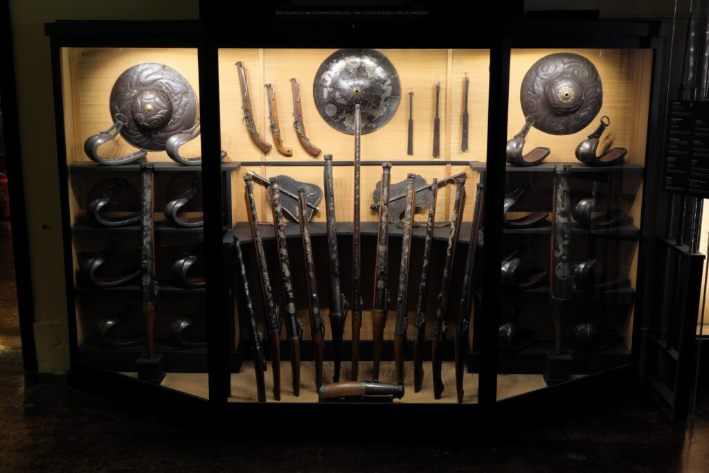 Vetrina con fucili, staffe e cappelli: vista d’insieme.